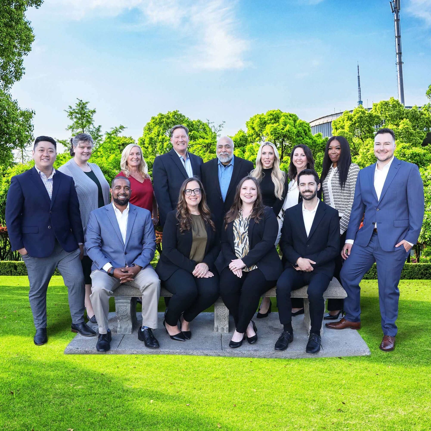 Group of professionals posing outdoors on a sunny day, dressed in business attire.