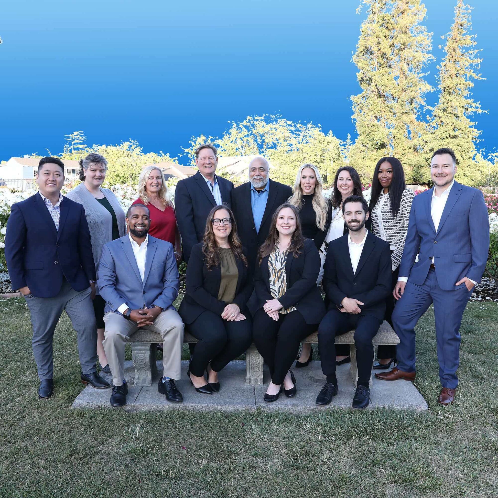 Group of professionals in business attire standing and sitting outdoors against a clear blue sky background.